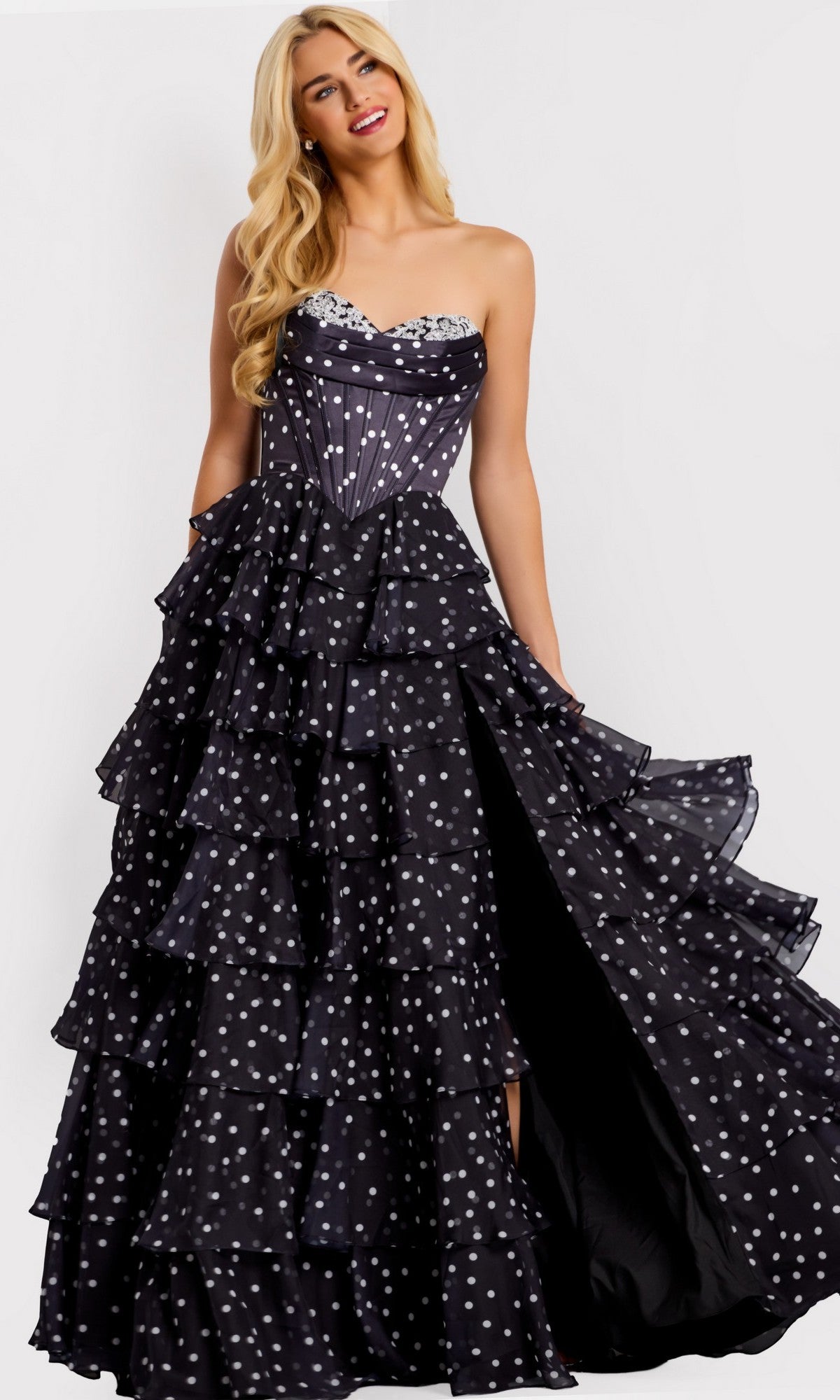 A woman in the Jovani 49087 long prom dress, featuring a strapless design with polka dots and tiered ruffle layers, stands against a plain background.